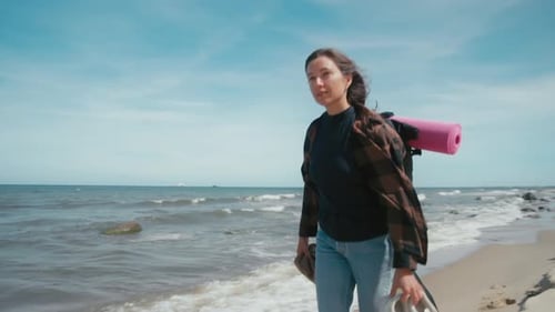Woman with backpack walks along a wild beach.