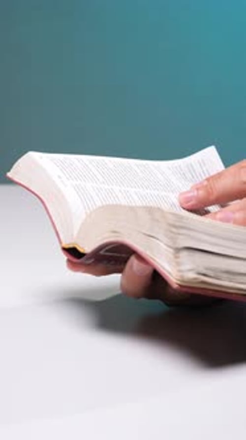 Vertical Video Person Holding a Thick Book with Both Hands Turning Pages and Reading the Text