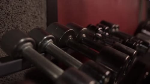 Weightlifting man takes dumbbells from storage rack in gym for fitness workout