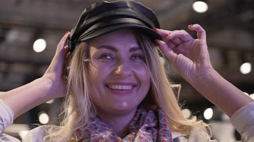 Smiling Women Customer Trying on Leather Hat in a Modern Luxury Shopping Mall