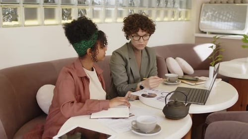 Colegas mujeres que trabajan con computadoras portátiles y papeles en un café