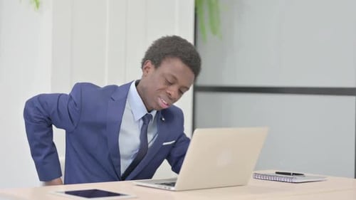 Man in Suit Typing on Laptop, Experiences Back Pain