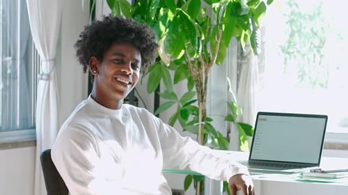 Smiling Young Adult Sitting near Laptop in Home