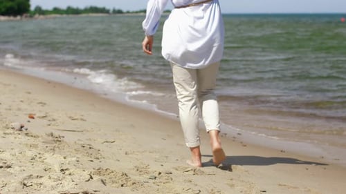 Middle aged woman enjoying summer vacation walking barefoot on the beach