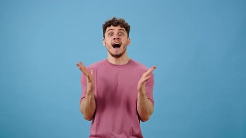 Young Caucasian Man Clenches Fists Screams in Anger on Blue Background Expressing Negative Emotion