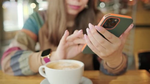 A Woman Intently Browses Her Phone a Cup of Coffee Nearby in the Inviting Ambience of a Local Cafe