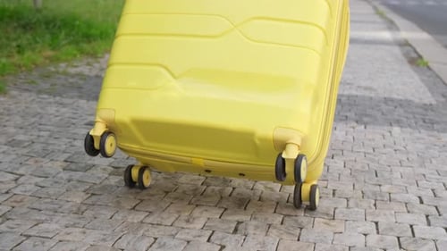 Closeup of a Yellow Suitcase Driving on Cobblestones in the City Traveling with a Suitcase