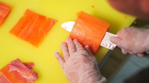 Hands in white gloves cutting pieces of fresh salmon fillet with big sharp knife. Close up.
