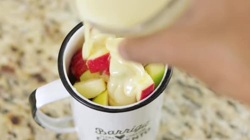 Condensed milk getting added to the fruit cocktail. Closeup.