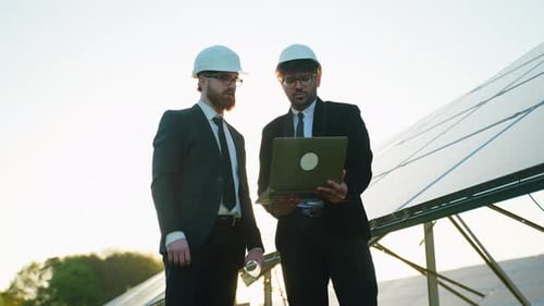 Engineers Discussing Data on Laptop Near Solar Panels