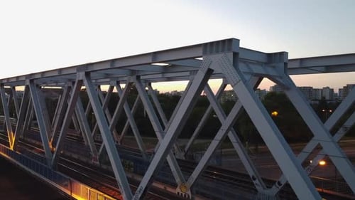 Aerial drone footage of a bridge while trains pass by on a sunset in Warsaw Poland with a city scape