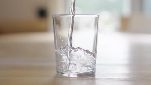 Statische Profilaufnahme in Zeitlupe, bei der Wasser in hinterleuchtetes Klarglas gegossen wird