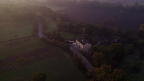 Aerial view of foggy countryside with road, field, trees, and houses, Italy.