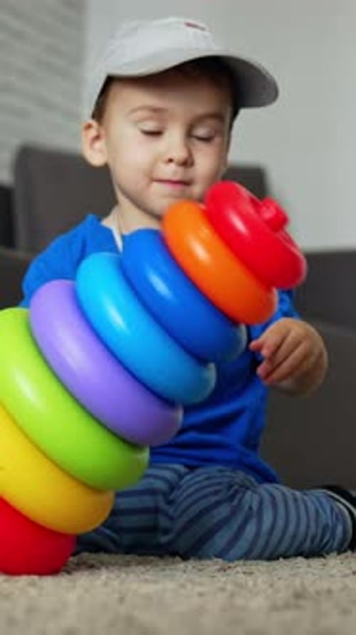 Un adorable niño pequeño tira su colorida pirámide al suelo.