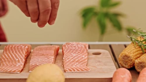Die Hände des Küchenchefs streuen vorsichtig Salz auf die Lachsfilets