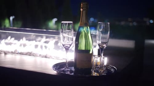 Champagne Bottle and Glasses by Fire Pit at Night