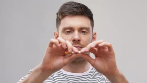 Un jeune homme casse une cigarette en deux, marquant ainsi la fin de sa dépendance au tabac