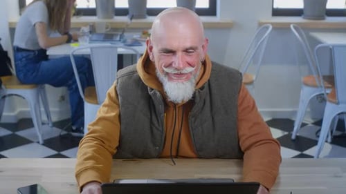 Stylish Old Man Conducts a Video Call in a Cafe or Restaurant with a Laptop Grandfather is a