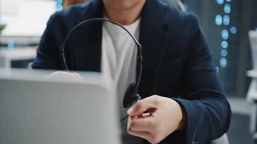 Nahaufnahme: Asiatischer IT-Entwickleradministrator, der mit Laptop einen Headset-Lautsprecher in der Hand hält und trägt