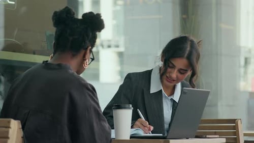Mujer birracial explicando conceptos comerciales a un colega, sentada al aire libre