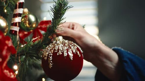 Person Decorating Christmas Tree with Red Ornament