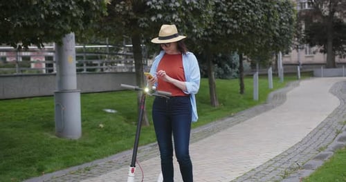 Woman Starts Electric Scooter with App on Phone in Park