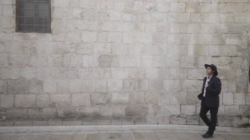 Un homme juif orthodoxe passe devant un vieux mur avec un livre dans la vieille ville de Jérusalem