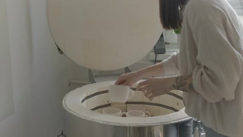 Woman Places Mugs into Kiln at Home