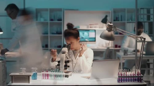 Young Female Intern with Microscope Analyzing New Chemical Substance