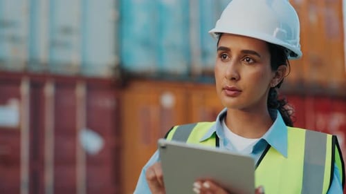 Beautiful Woman Stands In A Warehouse Dressed In Protective Uniform And Uses Tablet