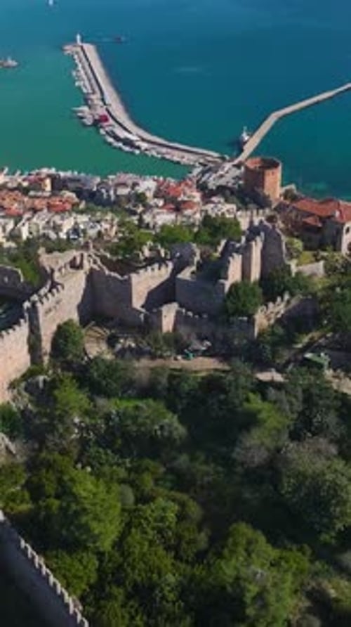 Vertikales Video: Szenische Luftaufnahme der Festung von Alanya, umgeben von viel Grün und mit Blick auf die