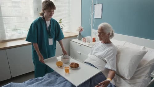 Young Medical Worker Serving Lunch for Senior Woman Sitting in Hospital Bed