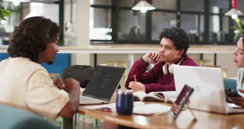 Étudiants afro-américains de sexe masculin à la table d'étude, penchés vers la gauche, tapant sur un ordinateur portable, clarifiant leurs devoirs
