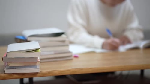 Student Writes in Notebook Surrounded by Books