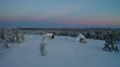Aerial view around pair of cabins on Scandinavian snow covered hilltop summit surrounded by wintry w