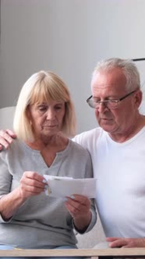 A Senior Couple Sits on the Couch in Their Cozy Living Room Reviewing Important Documents Together