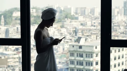 Woman Wrapped in Towel Using Phone Overlooking City