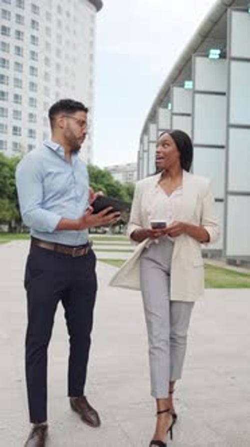 Vertical video of Two diverse business coworkers walk and discuss a project using a tablet in urban