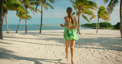 Frau läuft an sonnigen Tagen barfuß am tropischen Strand, umgeben von Palmen und Meer