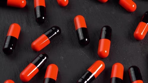 Many black and orange pills capsules or antidepressants rotating on black plate closeup low light