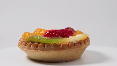 Pasteles giratorios con frutas sobre fondo blanco.