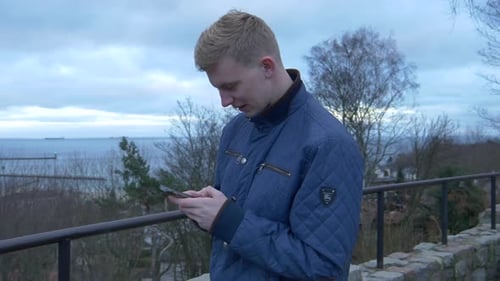 Paning shot on young blonde male writing sms on his smartphone with focused face
