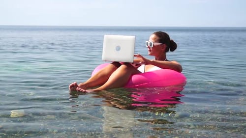 Woman Freelancer Works on Laptop Swimming in Sea on Pink Inflatable Ring Happy Tourist in Sunglasses