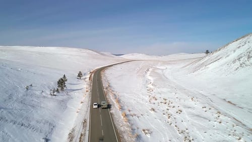 Aerial View on a Road Between the White Snowy Hills with Cars Driving on It Against the Blue Sky
