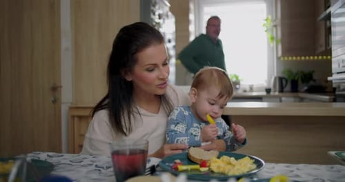 Mother Feeds Her Baby Breakfast at Kitchen Table