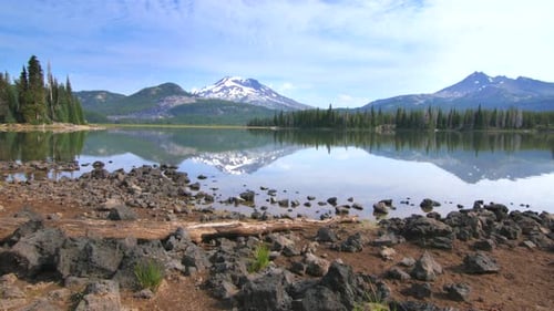 Bend Oregon lake reflects summer sky with snow capped mountains and forest