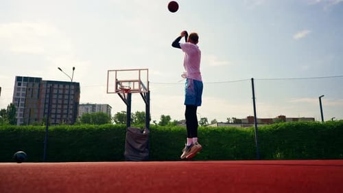 A tall guy basketball player throws a ball into a basketball hoop at a basketball court in the park