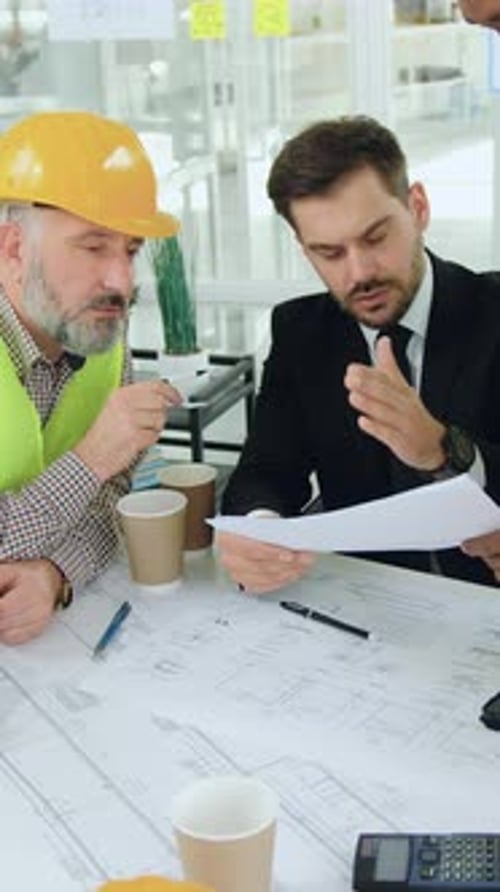 Attractive Highskilled Different Ages Multiracial Engineers Discussing Details of Building Draft
