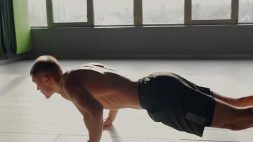 Focused Male Athlete Performing PushUps in Sunlit Gym