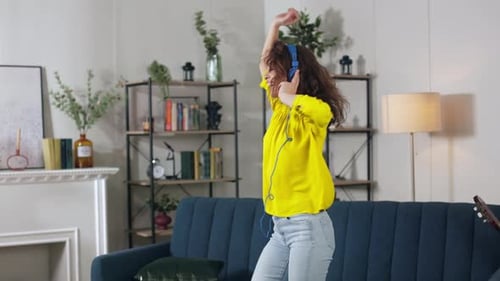 Woman with Headphones Dances Enthusiastically in Living Room